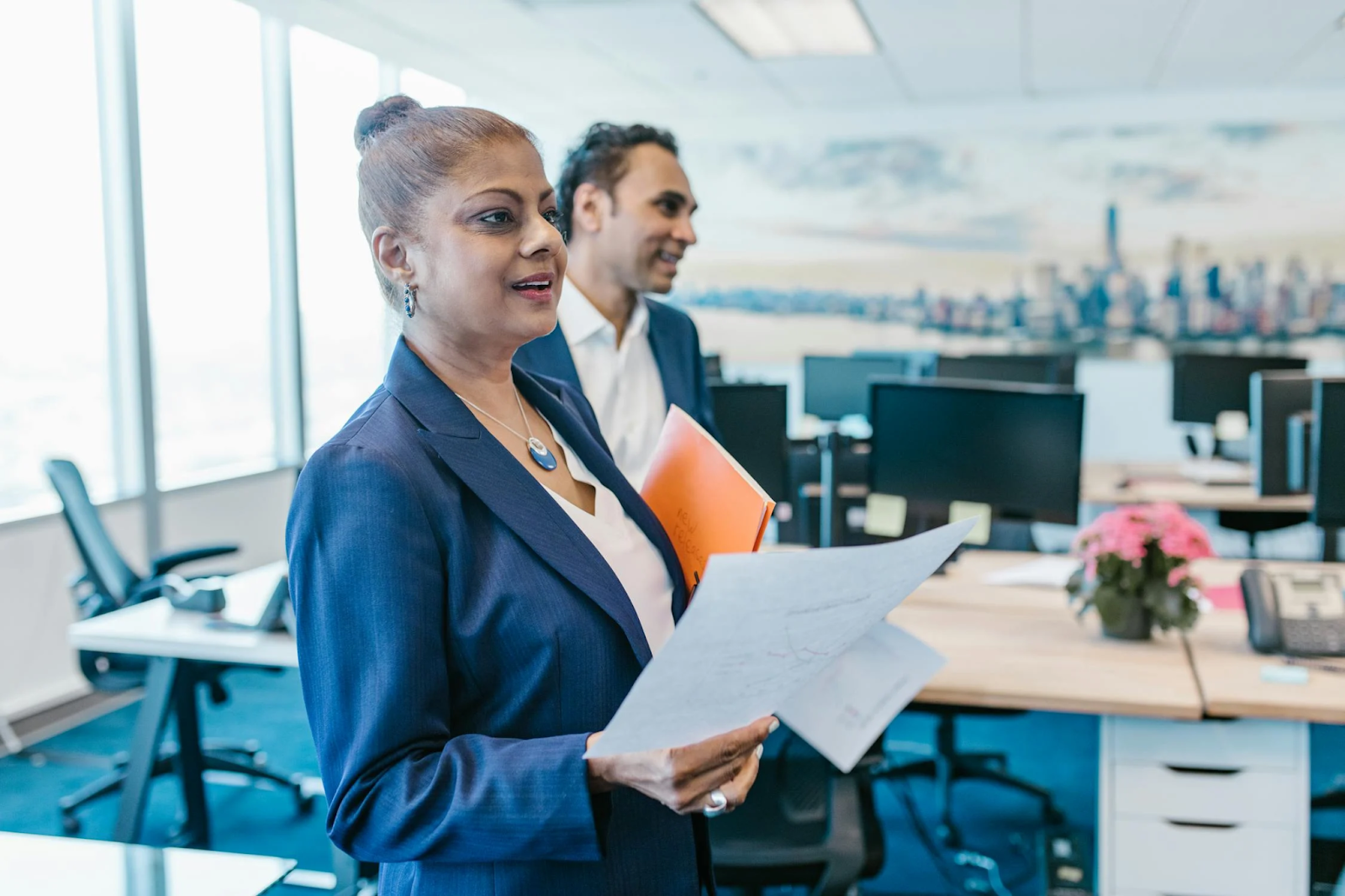 Two professionals, one woman and a man, in a modern office discussing a strategy, holding documents and folders—representing the blog’s protagonist Manisha who is looking for a robust strategy for small business marketing.
