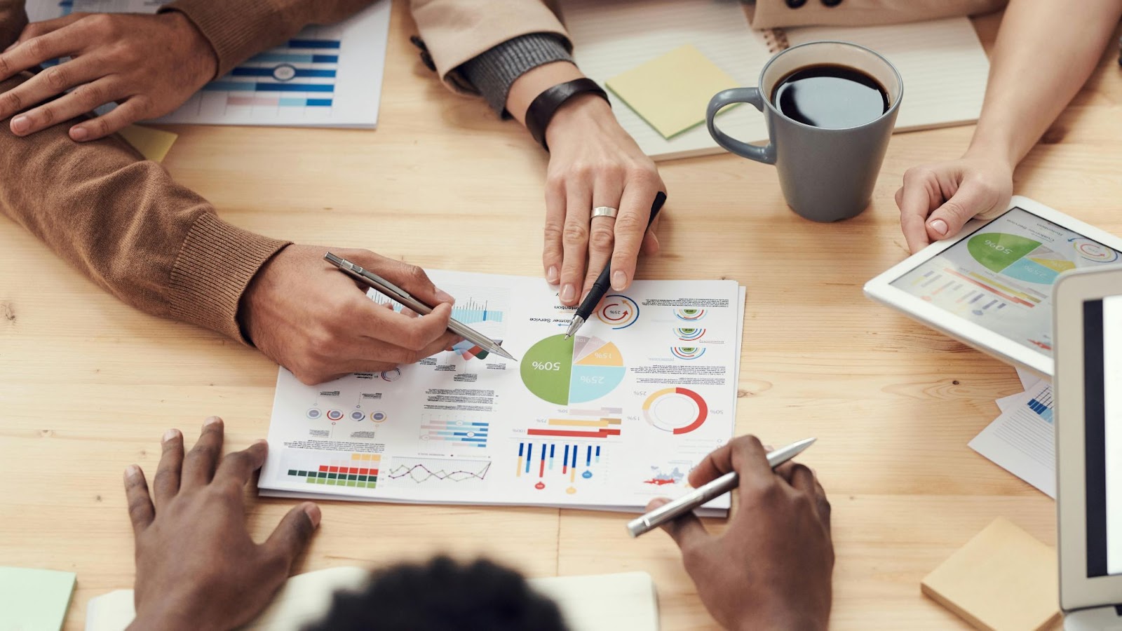 A close-up of a team analyzing colorful charts, graphs, and a tablet during a meeting, representing collaborative decision-making and data-driven strategies in small business marketing.