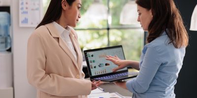 Woman employee shows charts on laptop to her boss, illustrating growth strategies with an alternative to enterprise SEO agency.