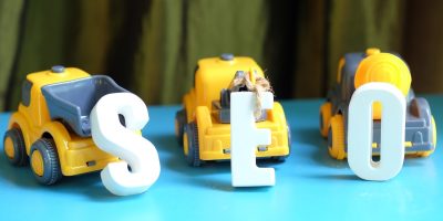 Three construction toy cars pulling blocks labeled “S,” “E,” and “O,” symbolizing how AI drives effective digital marketing for construction companies.