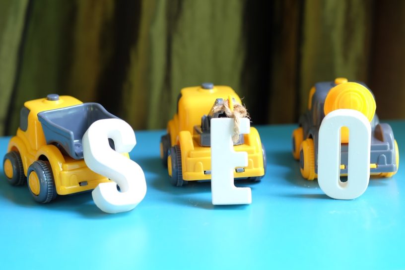 Three construction toy cars pulling blocks labeled “S,” “E,” and “O,” symbolizing how AI drives effective digital marketing for construction companies.